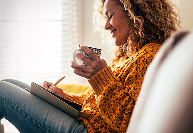 smiling woman sitting in chair with a cup of coffee and a notebook