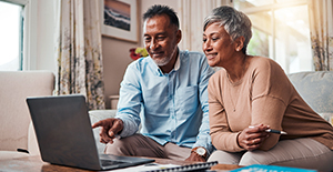 Mature couple sitting on sofa at home reviewing finances on laptop.